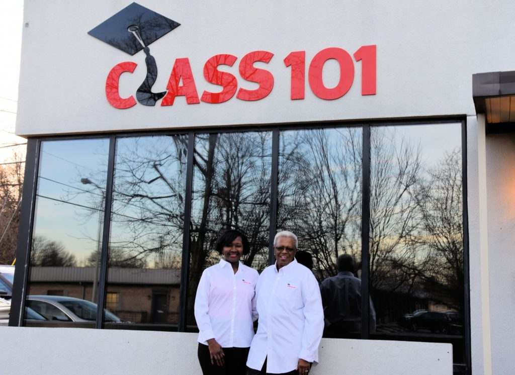 Two people smiling in front of Class 101 building